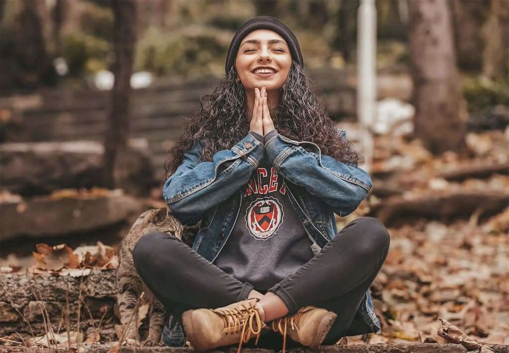 Mujer meditando al aire libre entre hojas otoñales.