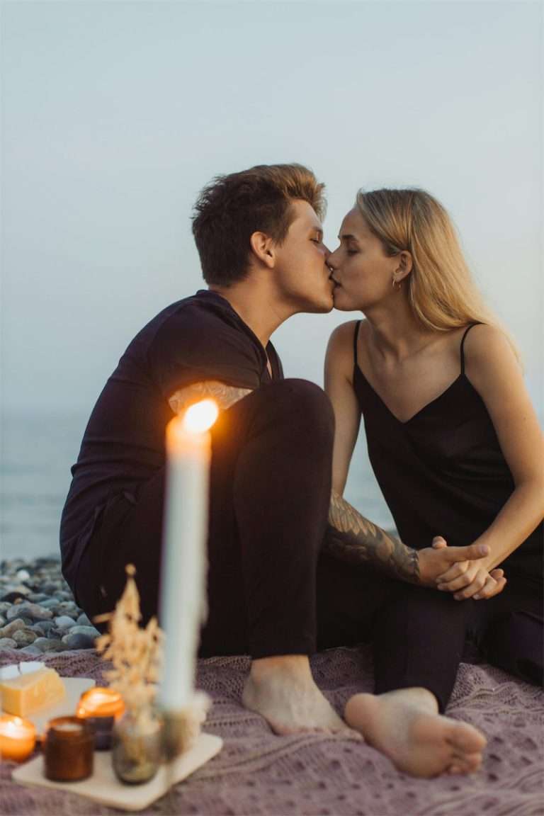 Two partners kissing by candlelight on a rocky beach at dusk